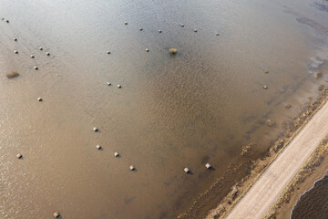 Flood in spring day. Gravel road. Hay rolls are located in flooded meadow water in spring. Aerial view.