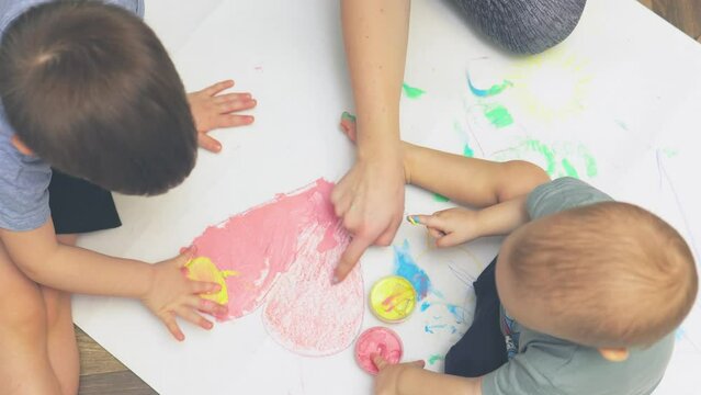 baby children drawing with finger paints pink heart white paper. mother teaching kids toddler painting using hand paint. early education home. unrecognizable child sitting on floor indoors coloring
