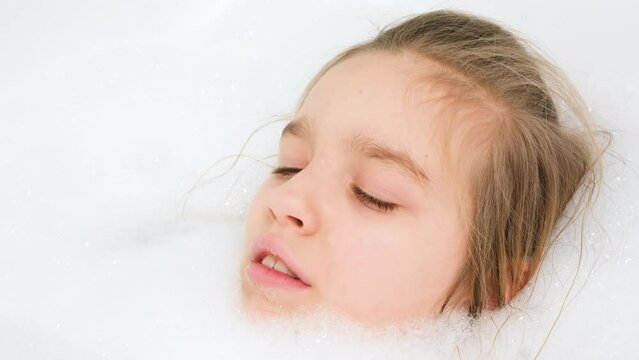 Portrait of cheerful teen girl lying in bath with thick soap foam and looking in camera. Concept of child hygiene and health care at home. Child having fun and playing at home.