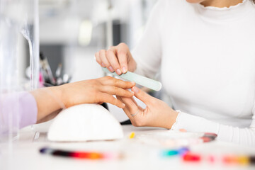 Young woman hands in a nail salon, which the manicure master files the nails with a nail file, giving them shape - obrazy, fototapety, plakaty