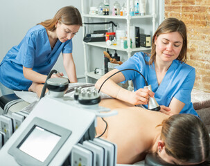 Fototapeta premium Two young professional masseuses working at the spa salon give the female client a relaxing massage using a devices