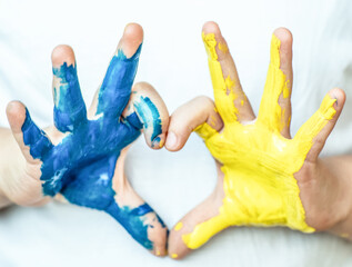 Children's hands painted in blue and yellow color in heart shape, flag of Ukraine. Stop war symbol. Ukrainian Independence Flag Day.