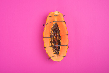 papaya cut in half surrounded by a wire on a pink background as a symbol of the vagina and pain in the intimate area