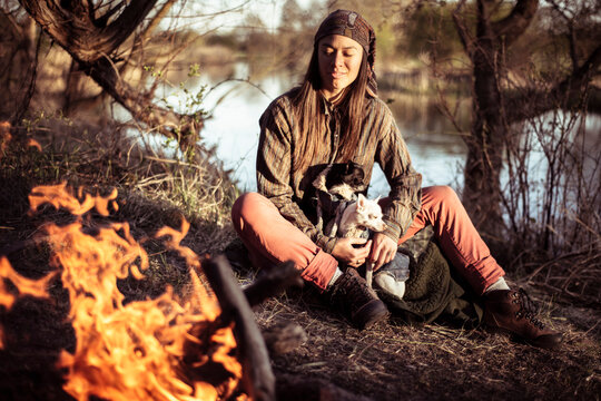 mixed race person in afternoon sun by water and fire with small dogs
