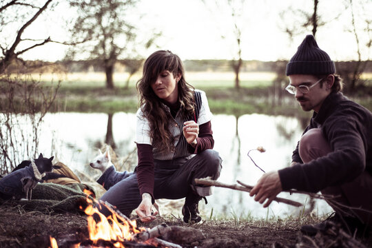 alternative friends gather around fire with dogs roasting marshmallows