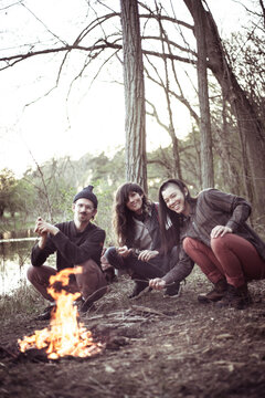 friends pose in front of fire by river and trees