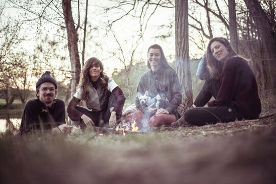 alternative friends sit around camp fire with small dogs