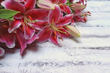 A large bouquet of bright pink lilies lies on a white wooden table. A postcard with flowers for a holiday, birthday, international Women's Day. Background for the gift package. Space for text.Close-up