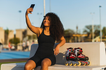 Chica marroquí morena con pelo rizado haciéndose selfie con smartphone en un espacio deportivo...