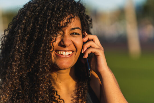 Chica joven marroqu&iacute; morena con pelo largo rizado hablando por tel&eacute;fono sentada junto a sus patines en linea