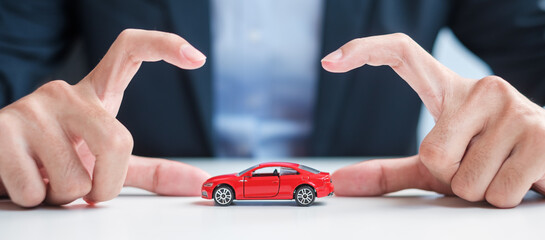 Businessman hand cover or protection red car toy on table. Car insurance, warranty, repair,...
