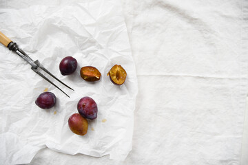 Food styling still life of plums with a vintage fork on a white table cloth