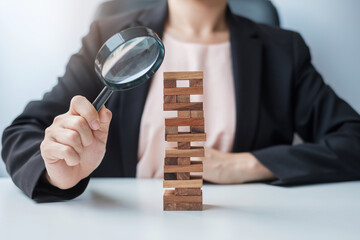 Businesswoman hand holding glass magnifying over wooden blocks tower. Business analysis, Risk...