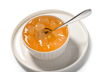 bright orange jelly with pieces of fruit in porcelain bowl with spoon inside close-up isolated on...