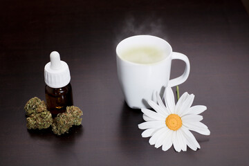 Obraz na płótnie Canvas marijuana buds with drops dispenser bottle, white cup with vapor infusion daisy flower ornament, on brown table, wooden background