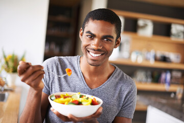 Have a bite of health. Indoor shot of a gorgeous young black man showing off his fruit salad.