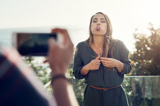 Shes always bringing out her inner child. Shot of an attractive young woman making funny faces while her boyfriend takes pictures of her outdoors.