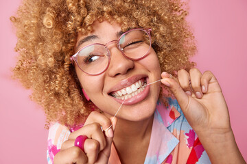 Close up shot of young woman with curly hair uses dental floss cleans teeth wears big optical...