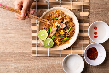 Thai food (Pad See Ew), Stir fried rice noodles with soy sauce, egg, kale and pork eating by use chopsticks, Table top view