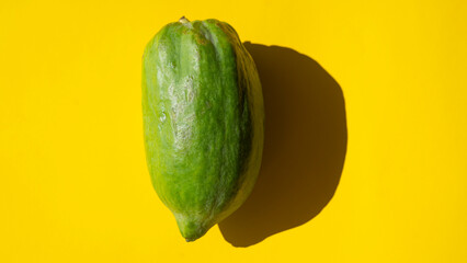 Whole green papaya on a yellow background with trendy hard shadow 