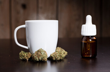 marijuana buds oil drop dispenser, and white cup, dark wood background