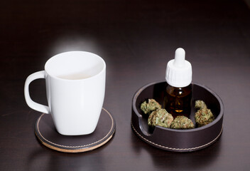 Obraz na płótnie Canvas white cup with infusion vapor, dropper bottle of marijuana oil drops, buds, on brown table, wooden background