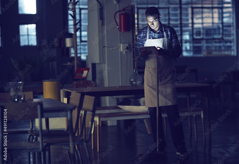 Poster Connected even while doing some chores. Shot of a young man working late on a digital tablet in his coffee shop.