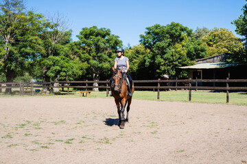 Obraz premium young latina woman in a stable riding a horse in the daytime, outdoor sports, horseback riding