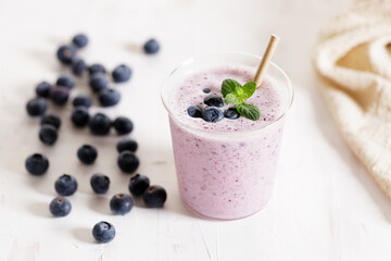 Fototapeta na wymiar Glass of blueberry milkshake with fresh blueberries on white wooden background.