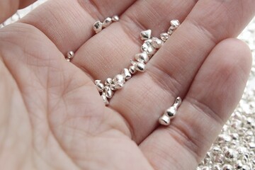 A white Caucasian person holds in hand grains of precious metal, precisely sterling silver which is important in stocks, jewelry and industrial use and gets expensive during crisis.