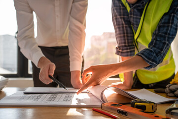Focused at the desk. behind is engineer and construction team leaders work together. View house designs and renovate plans. Construction projects. Mortgage, rent, buy, sell, move houses.