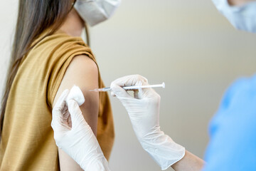 Asian woman wearing a medical mask receives coronavirus vaccine from a doctor. People are vaccinated against COVID-19 to prevent infection with the virus and stop its spread.