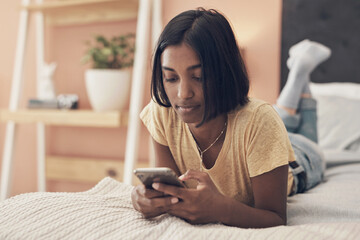 What would quarantine be without your social connection. Shot of a young woman using a smartphone while relaxing on her bed at home.