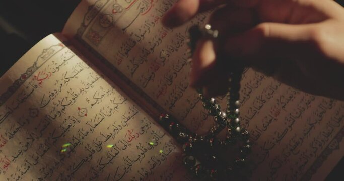Shot of an opened Quran and s person doing dhikr on his prayer beads