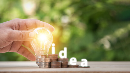 Man holding light bulb and many growth stack coins with plant in front and with the word Idea. concept saving money for finance accounting and idea for growing saving money.