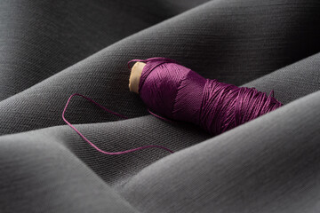 A spool with lilac threads in a draped soft gray fabric, close-up, macro. Atelier, tailoring,...