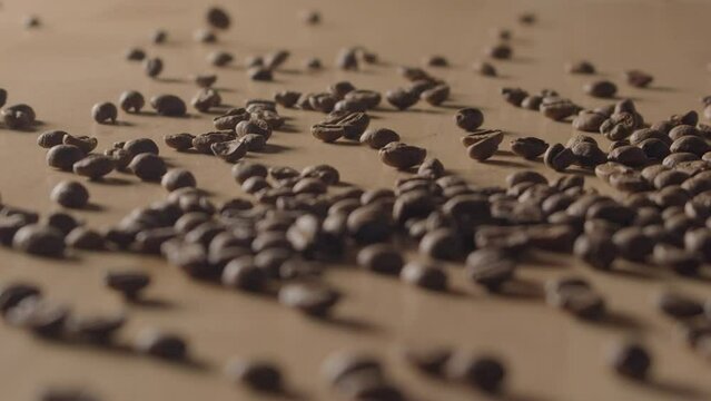 Smooth view of bunch of roasted coffee beans being poured into small pile. Top view of group of coffee grains scattered above wooden surface.