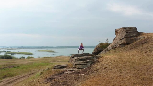 A girl is doing fitness on a hill on the lake shore