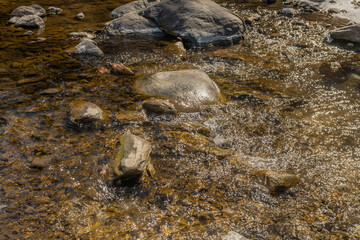 Closeup of water flowing around rocks and boulders on sunny winter day.