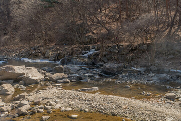 Winter landscape of mountain river with small waterfall on right side.