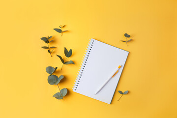Eucalyptus leaves and a notebook with a pencil on a yellow background. Top view. Flat lay. Place for text, copy space.