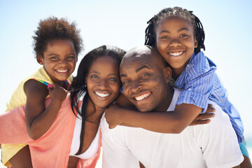 Its times like these you appreciate family. Two parents giving their children a piggyback while on the beach.