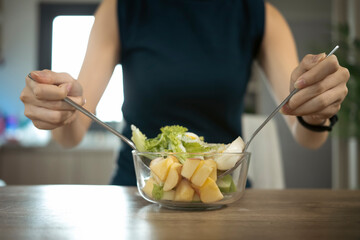 Cropped shot woman mixing fresh healthy vegan salad in glass bowl  in the kitchen at home.