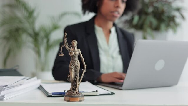 Young female lawyer typing on laptop and sitting at table with statue of justice in office spbi. 4k video Close view of beautiful businesswoman looks at computer screen and types text, does legal work