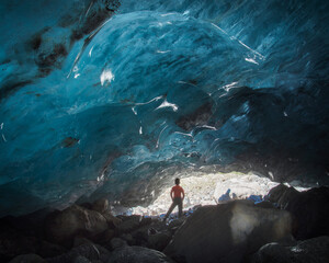 an ice cave in a mountain glacier with a teenager in an orange t-shirt