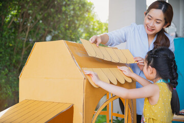 Children kids girls and mother hand making  paper house at home. Asian little child girl make and playing with cardboard house with her mom.