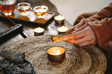 Woman hands burning Palo Santo, before ritual on the table with candles and green plants. Smoke of...