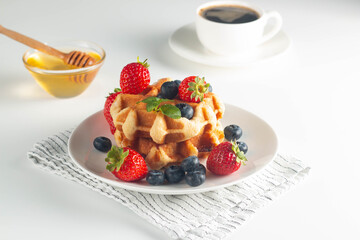 Fresh homemade food of berry Belgian waffles with honey, chocolate, strawberry, blueberry, maple syrup and cream. Healthy dessert breakfast concept with juice