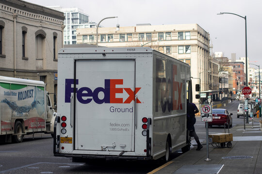 Portland, OR, USA - Jan 26, 2022: A FedEx Ground driver unloads his van and makes deliveries on the streets in the Pearl District of Portland, Oregon.