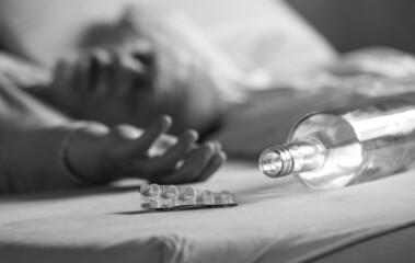Medicine and an empty bottle lie on a bed. In the background lies a man, he is sleeping.